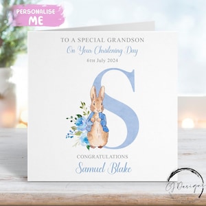 May include: A white christening card with the text "TO A SPECIAL GRANDSON On Your Christening Day 6th July 2024". Features a watercolor illustration of a rabbit, blue flowers, and the letter "S". The name "Samuel Blake" is printed below.