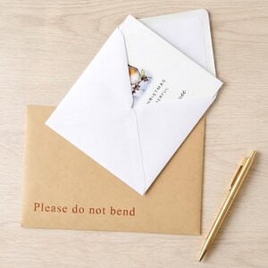 a brown envelope with a white card inside, along with a gold pen on a wooden surface. The text on the envelope reads "Please do not bend".