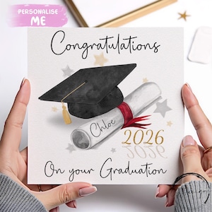 Może przedstawiać: Karta gratulacyjna z czarną czapką absolwenta, zwiniętym dyplomem przewiązanym czerwoną wstążką i napisem "Congratulations On your Graduation". Dyplom jest spersonalizowany imieniem "Chloe" i rokiem "2026".