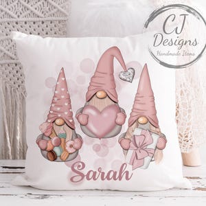 May include: White square cushion featuring three gnomes with pink hats and beards. One gnome holds a heart, another a gift, and the third holds sweets. The name "Sarah" is written in cursive below the gnomes. The cushion has the text "CJ Designs Handmade Items".