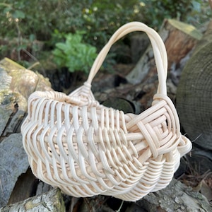 Peut inclure: Un panier en osier tressé avec une poignée, en osier naturel de couleur claire. Le panier est vide et a une forme arrondie.
