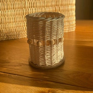 Peut inclure: Un porte-crayons en osier tressé avec une base en bois et une bande décorative de perles en bois.