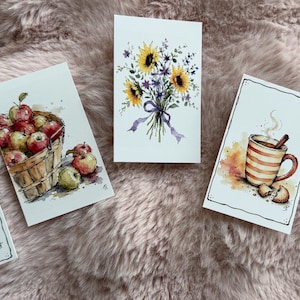 May include: Five rectangular cards featuring watercolor illustrations: a stack of three pumpkins, a wooden basket filled with red and green apples, a bouquet of yellow sunflowers, a steaming mug with a cinnamon stick, and a goose wearing a plaid coat.
