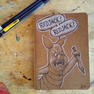May include: A brown paper notebook with a pencil drawing of a pig with a knife. The pig is looking angry and has the words "Redjack!" written above it.