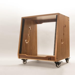 May include: A wooden audio equipment rack on wheels. The rack is constructed from light brown wood with a rectangular frame. It features curved handles and black metal strips with screw holes. The rack sits on four small black wheels.