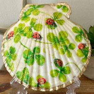 May include: A white seashell with a gold trim, painted with green four-leaf clovers and red ladybugs.