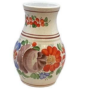 Puede incluir: Un jarrón de cerámica color crema con diseños florales pintados a mano. Presenta flores rojas, naranjas, azules y marrones con hojas verdes. Dos bandas marrones rodean el cuello. El jarrón tiene una base ancha y una parte superior ligeramente ensanchada.