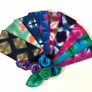 May include: A set of ten colourful tie-dye fabric squares arranged in a fan shape. The squares are made of cotton and have a variety of tie-dye patterns in shades of blue, green, pink, and purple. The fabric squares are rolled up in the centre of the fan.