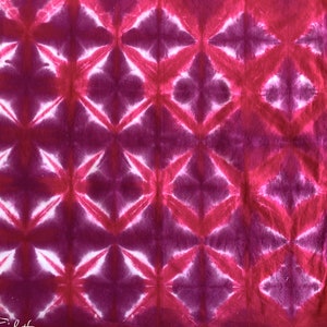 May include: A pink and white tie-dye fabric with a geometric pattern. The fabric has a repeating pattern of diamonds and stars.