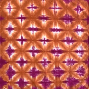 May include: A tie-dye fabric with a repeating pattern of orange and purple diamond shapes. The fabric has a white background.