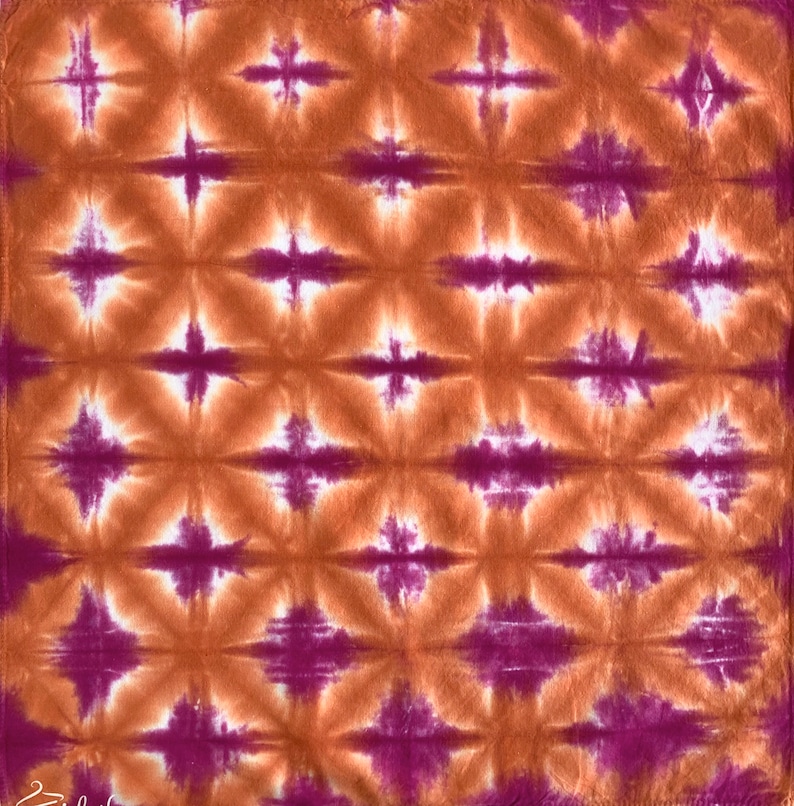 May include: A tie-dye fabric with a repeating pattern of orange and purple diamond shapes. The fabric has a white background.