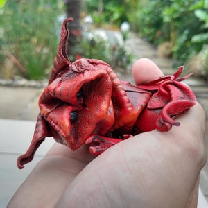 May include: A red leather creature with a long, pointed tail and large, expressive eyes. The creature is made of folded leather and has a textured surface.