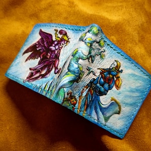 May include: A blue leather wallet with a hand-painted design featuring a winged figure in purple, a blue creature, and a woman with blonde hair in a blue dress.