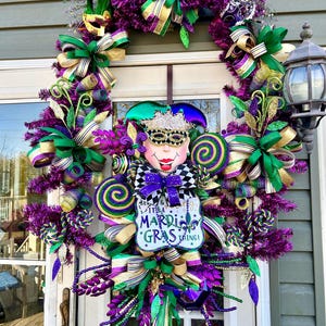 K&ouml;nnte beinhalten: Ein Mardi Gras Kranz mit lila, gr&uuml;nen und goldenen B&auml;ndern, einem Narrenkopf und einem Schild mit der Aufschrift "Be a King & It's a Mardi Gras Thing!"