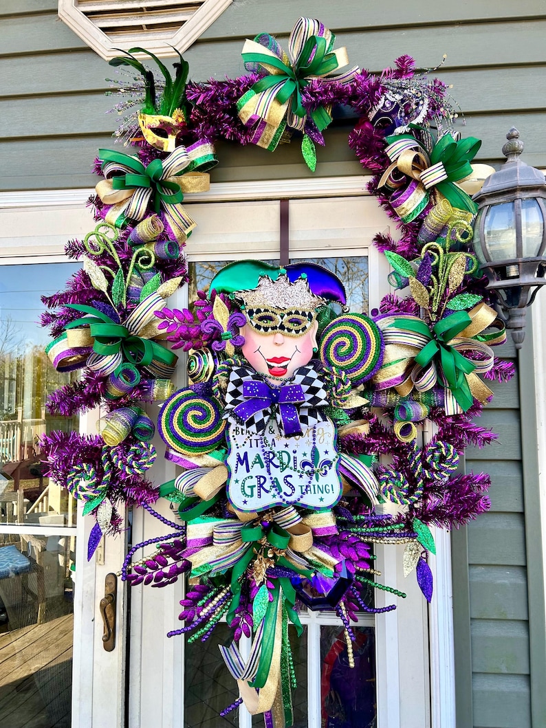 K&ouml;nnte beinhalten: Ein Mardi Gras Kranz mit lila, gr&uuml;nen und goldenen B&auml;ndern, einem Narrenkopf und einem Schild mit der Aufschrift "Be a King & It's a Mardi Gras Thing!"