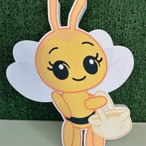 May include: A cartoon bee cutout with a yellow body, black stripes, and large eyes. The bee has white wings and is holding a light yellow basket. The letter "B" is in the bottom right corner.