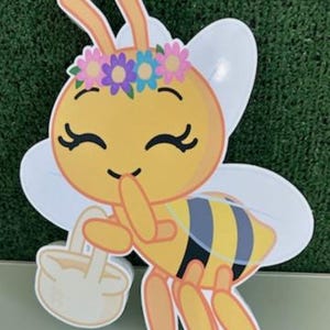 May include: A cartoon bee with a yellow body, black and yellow striped abdomen, and white wings. The bee wears a flower crown and carries a basket. The bee is smiling and has closed eyes. The letter "G" is in the bottom right corner.
