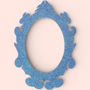 May include: A blue glitter oval frame with ornate scrollwork and a decorative top. The frame is set against a soft pink background, creating a contrast that highlights the frame's details. This decorative frame is ideal for home decor.