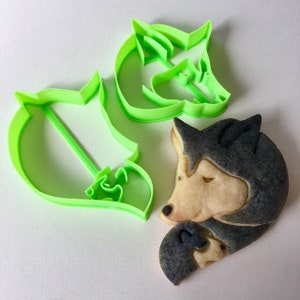 Puede incluir: Dos cortadores de galletas de plástico verde en forma de cabeza de lobo y lobo durmiendo, y una galleta decorada en forma de lobo durmiendo.