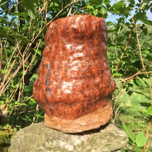 May include: A brown ceramic vase with a textured surface and a glossy finish. The vase has a rounded shape and a wide base.
