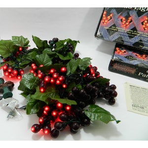 May include: A string of 100 miniature lights with grape clusters, designed to look like a grapevine. The lights are red and the grapes are dark purple. The packaging says "Gracious Living" and "100 Miniature Lights, 8 Grape Clusters".