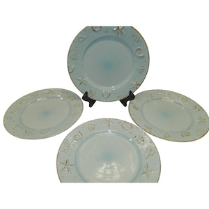 May include: Set of four light blue ceramic dinner plates with a raised seashell design in a gold color.