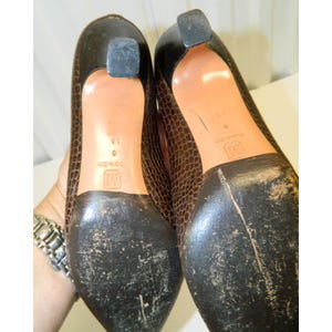 Op de afbeelding: Paar bruine pumps met slangenprint, spitse neuzen en zwarte hakken. De zolen zijn versleten. De hakken zijn ongeveer 5 cm hoog.