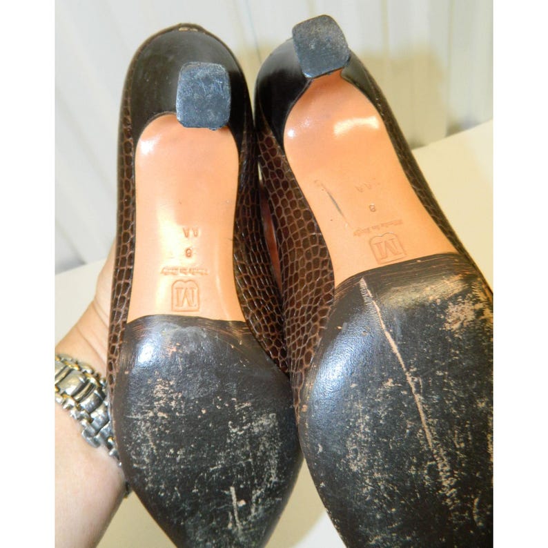 Op de afbeelding: Paar bruine pumps met slangenprint, spitse neuzen en zwarte hakken. De zolen zijn versleten. De hakken zijn ongeveer 5 cm hoog.