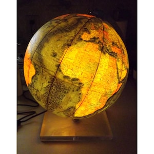 May include: A lit-up globe with a warm, yellow glow, showcasing continents and countries. The globe sits on a wooden base, with a power cord visible. The illuminated design highlights geographical features.