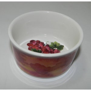 Könnte beinhalten: Eine weiße Keramik-Ramekin mit einem Trauben-Design. Die Ramekin hat einen aquarellartigen Hintergrund in Rosa-, Orange- und Gelbtönen. Die Trauben sind in Rot- und Violetttönen bemalt.