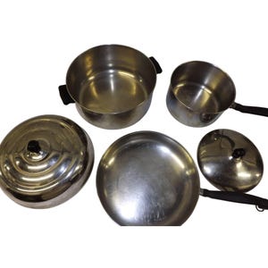 May include: A collection of stainless steel cookware, including a large pot with black handles, a saucepan, a frying pan, and two lids. The set is arranged on a white surface, showcasing the reflective quality of the metal.