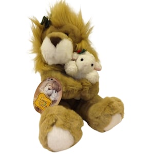 May include: A plush lion holding a plush lamb. The lion has a brown mane, white face, and white paws. The lamb is white with a red and green accent. A tag with the words "The Lion and the Lamb" is attached.