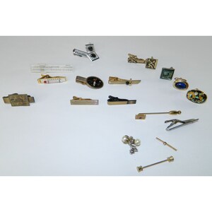 May include: A collection of vintage tie clips and cufflinks. The tie clips are made of gold and silver metal and feature various designs, including a golfer, a compass, and a striped pattern. The cufflinks are made of gold and silver metal and feature various designs, including a golfer, a compass, and a striped pattern. There are also two pairs of pearl earrings.