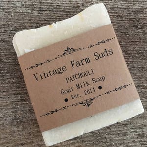 Op de afbeelding: Een staaf witte geitenmelkseep met een bruin papieren etiket waarop staat "Vintage Farm Suds Patchouli Goat Milk Soap Est. 2014".