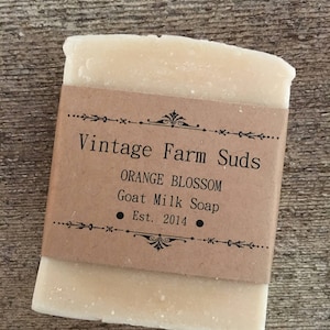 May include: A bar of goat milk soap wrapped in brown paper with the text "Vintage Farm Suds", "Orange Blossom", "Goat Milk Soap", and "Est. 2014".