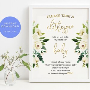 May include: A white frame with a gold floral design and the text "PLEASE TAKE A clothespin hold on to it tight, try not to say baby with all of your might when you hear someone say baby snatch up their pin if you have the most at the end then you WIN!"