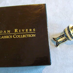 May include: A gold-toned ribbon brooch with navy blue enamel detailing and clear crystal rhinestones. The brooch sits beside a black box with gold text reading "Joan Rivers Classics Collection".