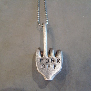 May include: A silver necklace with a pendant shaped like a middle finger with the words "FORK OFF" engraved on it.