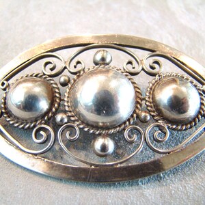 Puede incluir: Un broche de plata con tres círculos redondos de plata en relieve en un diseño de filigrana.