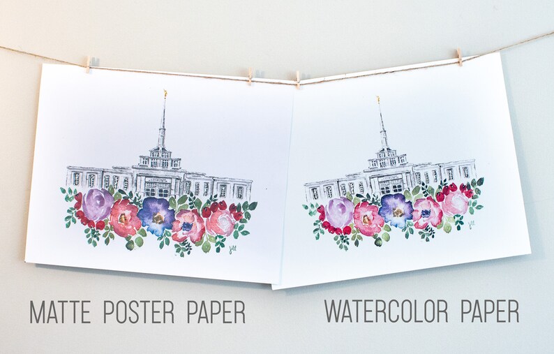 May include: Two prints of a watercolor illustration of a building with a steeple and a floral wreath at the bottom. The print on the left is on matte poster paper and the print on the right is on watercolor paper. The text "MATTE POSTER PAPER" is below the left print and the text "WATERCOLOR PAPER" is below the right print.