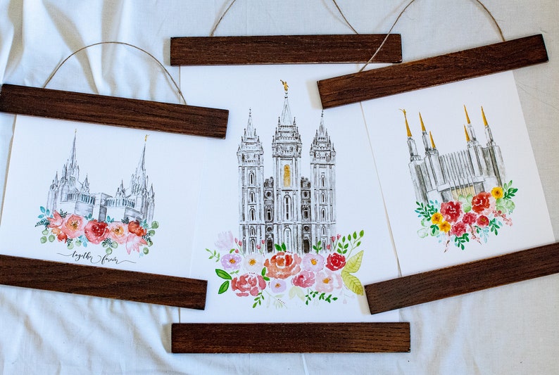May include: Three watercolor prints of different temples with floral arrangements at the bottom. The prints are framed with dark wood and hung with twine.