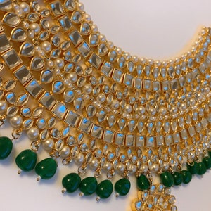 Puede incluir: Un collar dorado y blanco con cuentas verdes. El collar tiene varias capas de piedras doradas y blancas y está decorado con cuentas verdes.