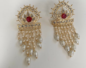 May include: Gold earrings with a red stone and pearl drop. The earrings have a detailed design with a heart shape and a row of small stones.