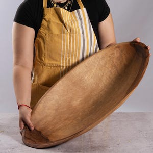 Puede incluir: Un cuenco de madera grande de forma ovalada con un interior liso de color marr&oacute;n claro y un patr&oacute;n de veta de madera natural m&aacute;s oscuro a lo largo del borde exterior. El cuenco presenta una cuenca profunda y alargada con un acabado pulido que resalta la textura org&aacute;nica.