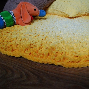 May include: A yellow and white crocheted rug with a gradient pattern. The rug is round and has a soft, fluffy texture.