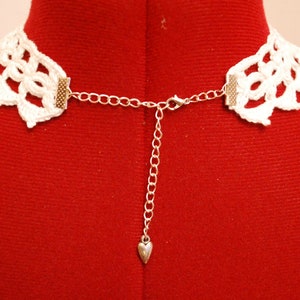 May include: White crocheted choker necklace with a silver chain and heart charm.