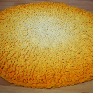 May include: A round, yellow and white bath mat with a gradient pattern. The mat is made of a soft, fluffy material.
