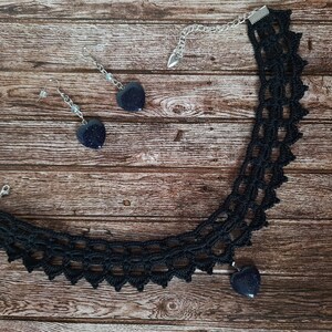 May include: A black crocheted choker necklace with a heart-shaped pendant and matching earrings. The pendant and earrings are made of dark blue stone.
