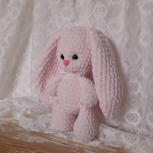 K&ouml;nnte beinhalten: Ein rosa geh&auml;keltes Pl&uuml;sch-Hasenspielzeug mit gro&szlig;en Ohren. Der Hase hat schwarze Augen und eine rosa Nase.