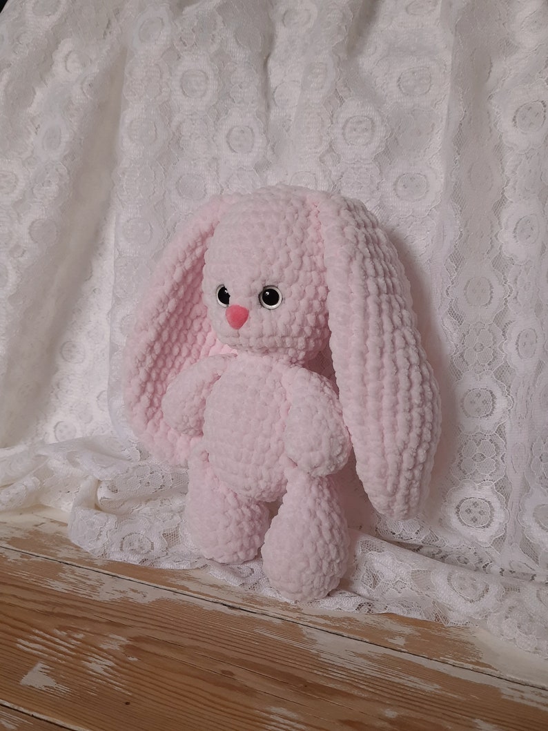 K&ouml;nnte beinhalten: Ein rosa geh&auml;keltes Pl&uuml;sch-Hasenspielzeug mit gro&szlig;en Ohren. Der Hase hat schwarze Augen und eine rosa Nase.